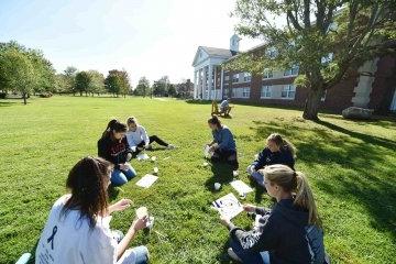 一群学生盘腿坐在草地上做绘画作业.